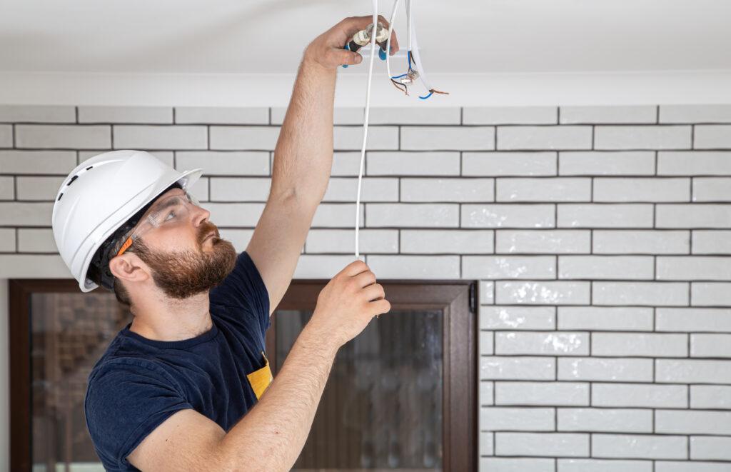 Electrician Builder at work, installation of lamps at height. Professional in overalls with an electrical tool. On the background of the repair site. The concept of working as a professional.